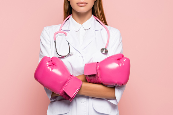 Cropped näkymä lääkäri valkoinen takki ja vaaleanpunainen nyrkkeily käsineet seisoo ristissä kädet eristetty vaaleanpunainen - Valokuva, kuva