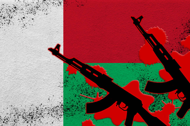 Bandeira de Madagáscar e dois fuzis AK-47 pretos a sangue vermelho. Conceito para ataque terrorista ou operações militares com resultado letal. Uso de armas perigosas - Foto, Imagem