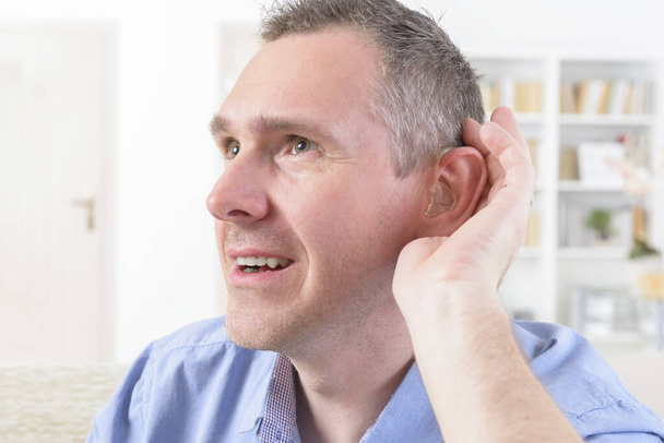 Muž s hluchou pomůckou v uchu se pokouší něco zaslechnout - Fotografie, Obrázek