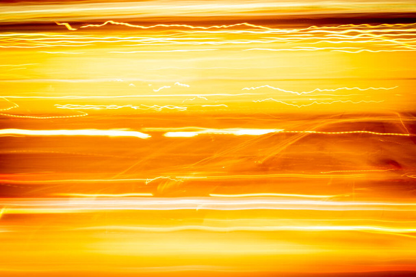 Длительная экспозиция желто-оранжевый свет фотография, рябь и линии на черном фоне. Вид на городские огни из окна скоростного поезда. - Фото, изображение