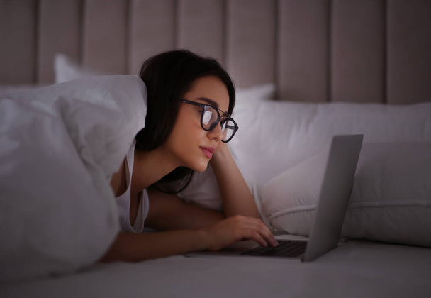 Young woman with nomophobia using laptop in bed at night. Insomnia concept - Photo, Image