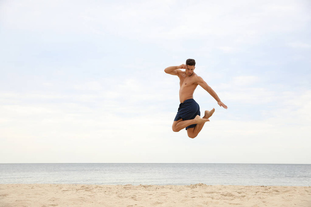 Muscular man jumping on beach, space for text. Body training - Foto, Imagen