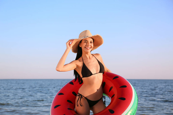 Schöne junge Frau im schwarzen stylischen Bikini mit aufblasbarem Ring am Strand - Foto, Bild