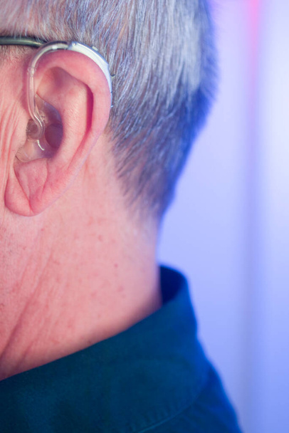 Λευκός Καυκάσιος ηλικιωμένος άνδρας με σύγχρονο ψηφιακό ακουστικό στο αυτί με γκρίζα μαλλιά. - Φωτογραφία, εικόνα