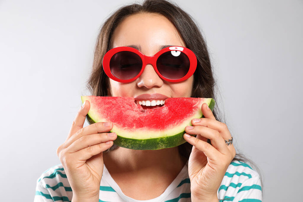 Beautiful young woman eating watermelon on grey background - Foto, imagen