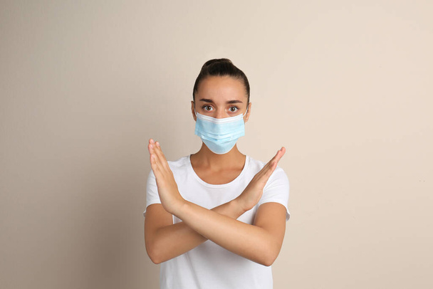 Woman in protective mask showing stop gesture on beige background. Prevent spreading of COVID?19 - Foto, Bild