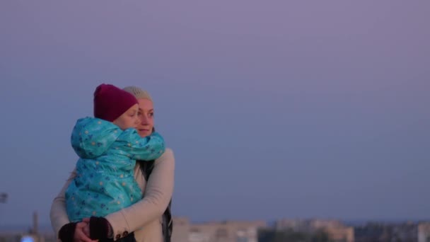 Мати і дочка стоять у вечірньому міському ландшафті. Маленька дівчинка обіймає і цілує маму на заході сонця. Любляча дитина обіймає маму. Сімейна листівка до Дня матері. Життєпис 4K - Кадри, відео