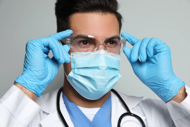 Doctor in protective mask, glasses and medical gloves against light grey background - Foto, Imagen
