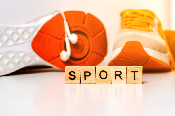 Sneakers sportive e manubri arancioni su sfondo bianco con lettere in legno "sport", concetto di fitness - Foto, immagini
