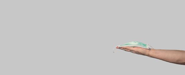 Прапор з медичною маскою для обличчя, запропонованою триманням особистої долоні як запобіжний захід від спалаху пандемії коронавірусу у всьому світі з копіювальним простором для тексту на твердому сірому фоні, деталі, крупним планом
 - Фото, зображення