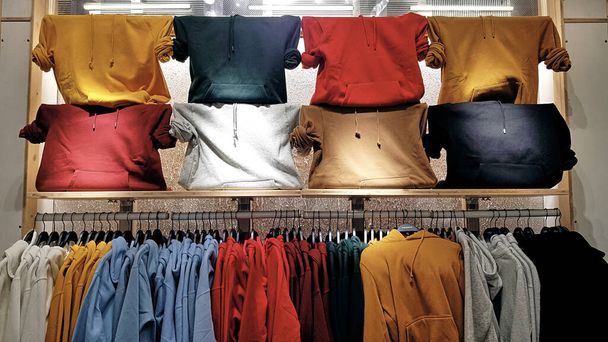 Jasne, kolorowe bluzy wiszące w sklepie z modą. Zbliżenie wielobarwnych żółtych, czerwonych, różowych, geen bluz wiszą w rzędzie na wieszaku w sklepie odzieżowym w centrum handlowym. - Zdjęcie, obraz