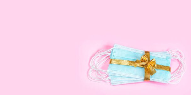Medizinische Schutzmasken mit goldenem Band isoliert auf rosa Hintergrund. Ein Geschenk zu Weihnachten und Neujahr 2021. Coronavirus-Pandemiekonzept. Banner. - Foto, Bild