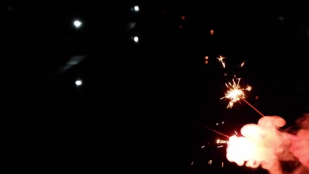 Langzame videoclip van een gele korst spetterend van vuurwerk in de hand en witte rook drijvend op een zwarte achtergrond. - Video
