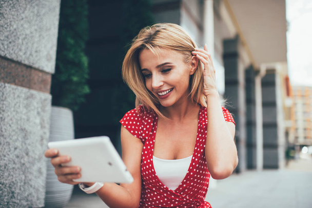 Happy millennial girl enjoying online networking via modern touch pad sitting at urbanity and feeling happiness with social web resting, cheerful user watching positive video streams on website - Fotó, kép