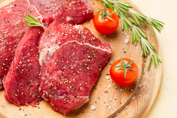 Slices of meat in salt and pepper, rosemary and tomatoes - Foto, afbeelding