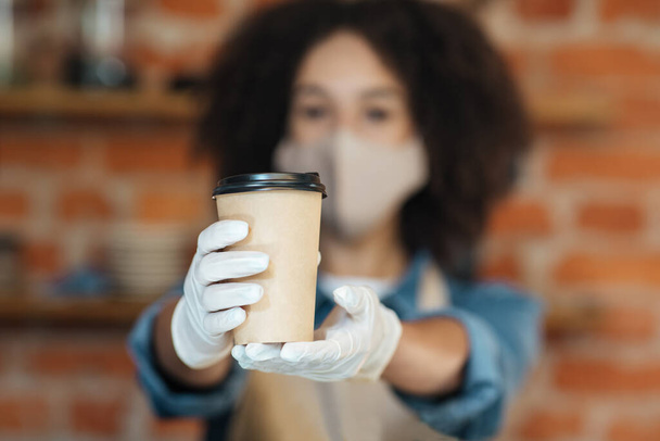 Frau mit Gesichtsmaske serviert Kaffee im Covid-19, soziale Distanzierung, kleines Coffeeshop-Geschäft und Virusprävention - Foto, Bild