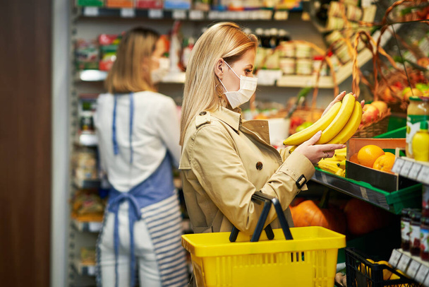 Volwassen vrouw in medisch masker winkelen voor boodschappen - Foto, afbeelding
