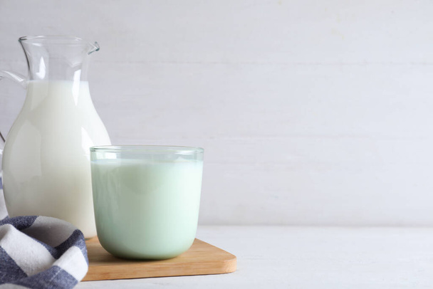 Jug and glass with fresh milk on white wooden table. Space for text - Foto, afbeelding