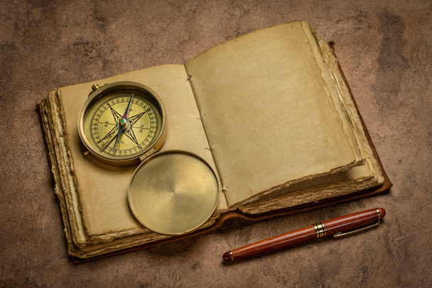 antique leather-bound journal with decked edge handmade paper pages  on a rustic wooden table with a stylish pen and vintage brass compass, journaling concept - Foto, immagini