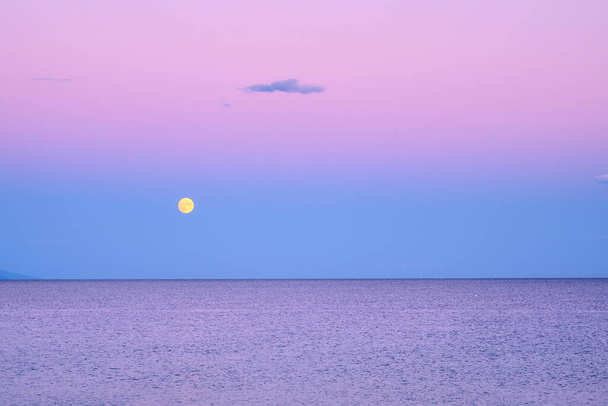 Ciemnofioletowe niebo z żółtym księżycem nad morzem po zachodzie słońca w Grecji - Zdjęcie, obraz