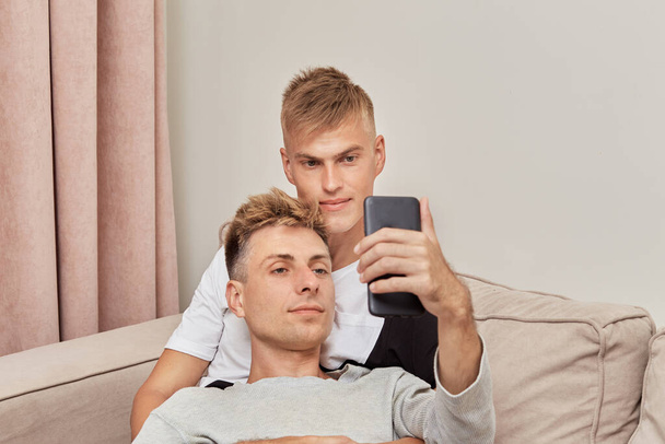 Beautiful men gay couple bloggers taking selfies on their smartphone. - Фото, изображение