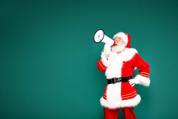 Authentic Santa Claus with white beard screaming through megaphone on a green studio background. A lot of copy space for your sample text. Merry Christmas and Happy New Year concept. - Фото, зображення
