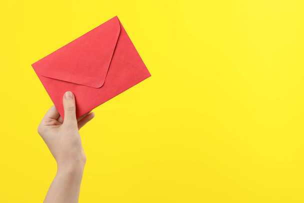 Woman holding red paper envelope on yellow background, closeup. Space for text - Foto, Imagem