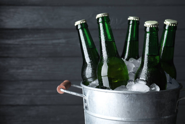 Metal bucket with bottles of beer and ice cubes on dark wooden background, closeup. Space for text - Valokuva, kuva