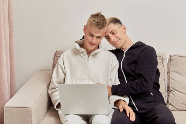 Dos amantes de los hombres sentados en casa en pijama se comunican en línea. - Foto, imagen