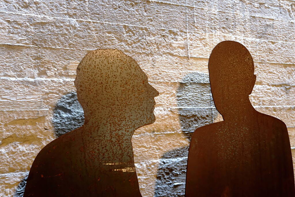 Zwei rostige Metallplatten als menschliche Silhouette auf einem rauen Betonwandhintergrund. Silhouette von zwei Menschen.                                - Foto, Bild