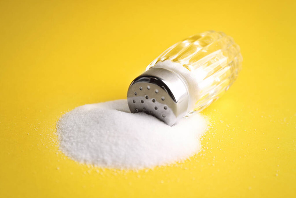 Scattered salt and shaker on yellow background, closeup - Foto, imagen