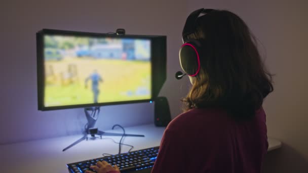 Teenage girl sitting in front of a computer, playing a game wearing a headset - Footage, Video