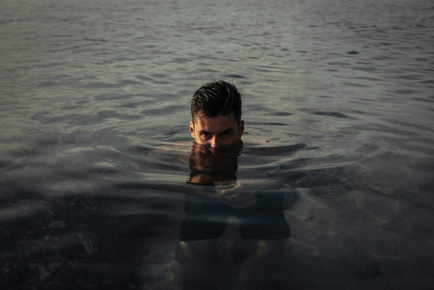Ένας όμορφος άντρας στέκεται στη μέση του νερού στην παραλία. - Φωτογραφία, εικόνα