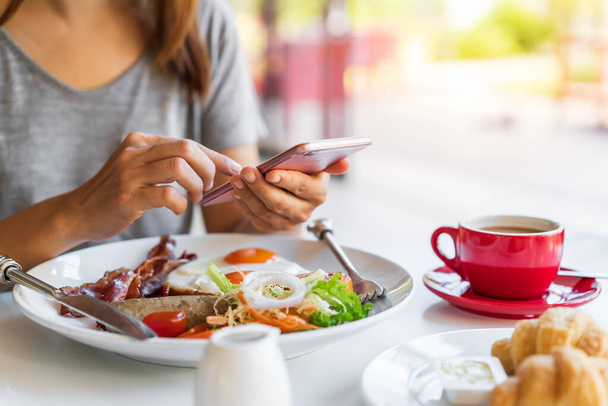 Молодая женщина, используя смартфон с чашкой кофе за завтраком - Фото, изображение
