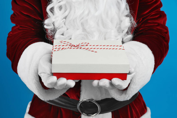 Santa Claus holding Christmas gift on blue background, closeup - Fotó, kép
