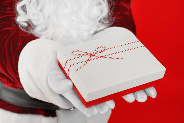 Santa Claus holding Christmas gift on red background, closeup - Fotoğraf, Görsel