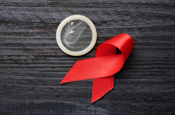 Red ribbon and condom on black wooden background, flat lay. AIDS disease awareness - Foto, Imagen
