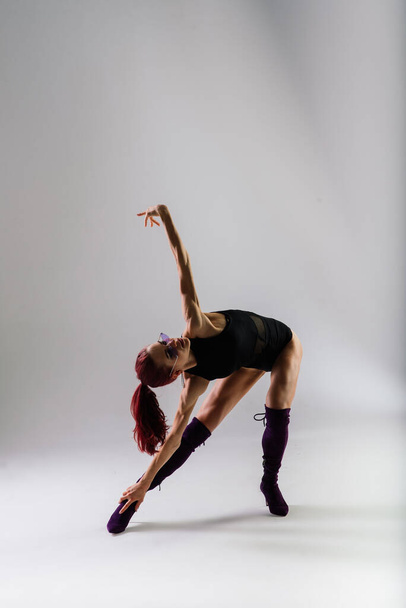 jong mooi flexibel vrouw in een zwart jumpsuit en hoge hakken is poseren in een dans studio. - Foto, afbeelding