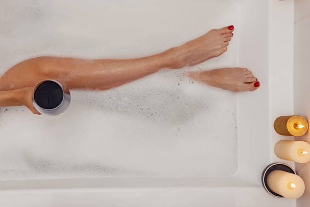 Woman drinking red wine while taking bath with foam - Foto, afbeelding