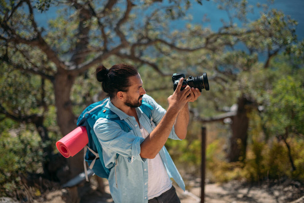 Mies turisti, valokuvaaja vuoristossa lehto merinäköalalla. Nuori komea kaveri turisti reppu ja kamera näkökulmasta puissa ja tarkastellaan luonnonkaunis näkymä merelle - Valokuva, kuva