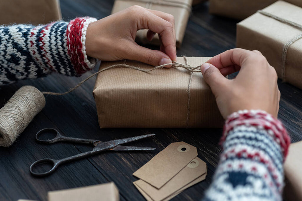 Руки женщины в свитере, обволакивающем рождественскую подарочную коробку, украшенную крафтовой бумагой - Фото, изображение