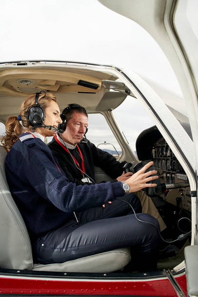 Pilote en formation et instructeur de vol dans le poste de pilotage d'un avion. Portrait de jeune pilote séduisant avec écouteurs se préparant à voler. Il est assis à côté de la femme instructrice et regarde le tableau. - Photo, image