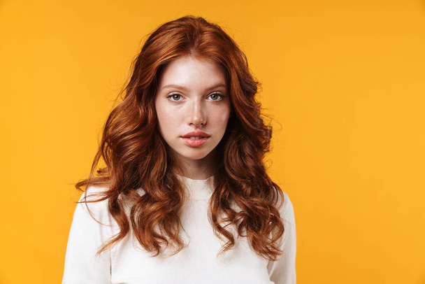 Image of ginger beautiful girl posing and looking at camera isolated over yellow background - Fotó, kép