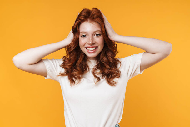 Image of ginger joyful girl smiling and grabbing her head isolated over yellow background - Fotografie, Obrázek