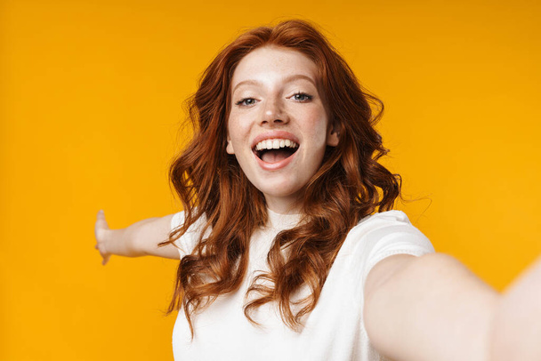 Image of redhead cheerful girl showing cpyspace and taking selfie photo isolated over yellow background - Fotoğraf, Görsel