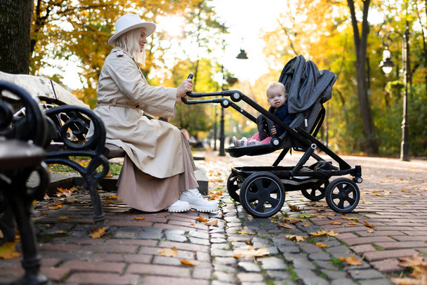 Moeder zitten op een bank en schommelen de baby in een wandelwagen - Foto, afbeelding