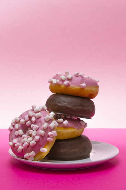 Close-up of a hand picking up a donut from a white plate of pink donuts with cumin and chocolate covered. Horizontal photography - Foto, Imagem