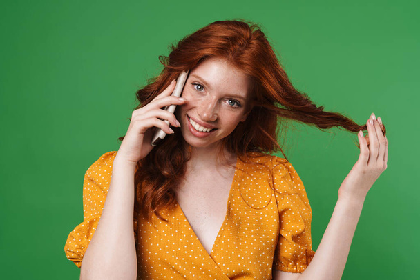 Image of ginger happy girl smiling and talking on mobile phone isolated over green background - Φωτογραφία, εικόνα
