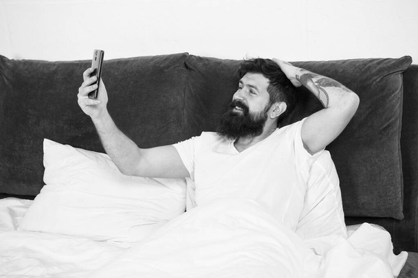 Selfie first thing in the morning. Bearded man take selfie in bed. Happy hipster smile to camera phone. Video selfie. Selfie for blog. Social network. Weblog. Modern life. New technology - Φωτογραφία, εικόνα