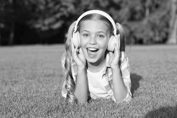 small girl listen audio book. new technology for kids. happy childhood memories. listening to music. back to school. kid study in park. relax on green grass in headphones. Hooked On Learning. - Fotó, kép